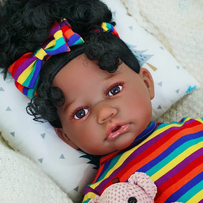 The second image is a close-up of the baby doll's face, highlighting its expression. The doll is wearing a matching rainbow-striped headband and holding the teddy bear.