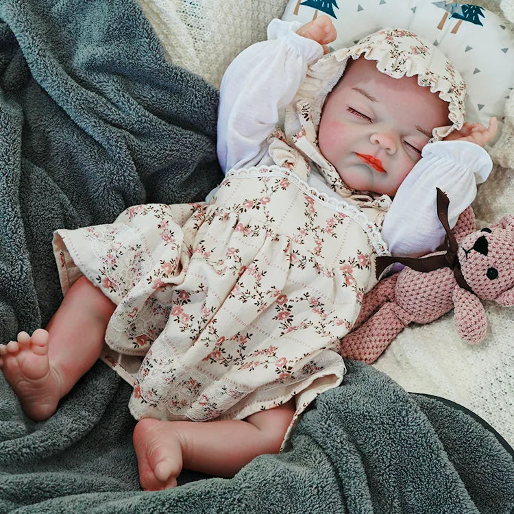 The reborn baby doll stretching out in a relaxed position, wearing a floral outfit and bonnet, cuddling with a soft teddy bear.