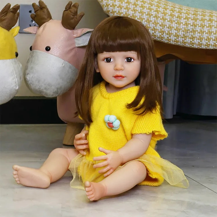 The toddler doll sitting on a colorful couch, legs crossed, still in the yellow dress, showing more of the background.