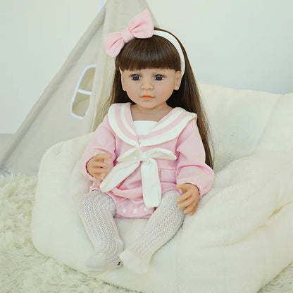 Reborn doll in pink outfit sitting on a chair.