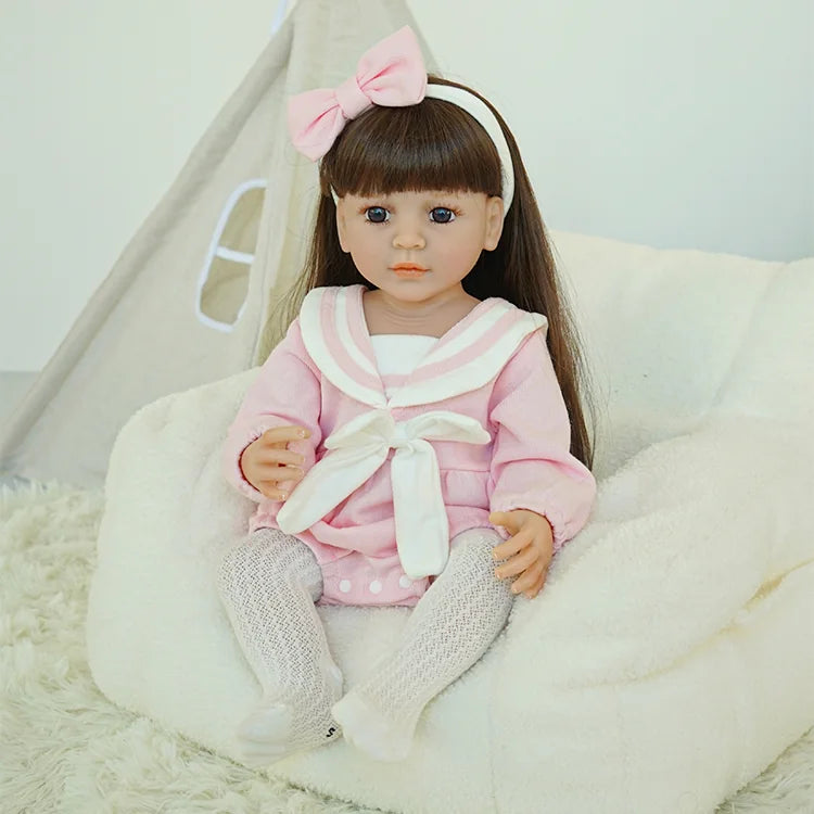 Reborn doll in pink outfit sitting on a chair.