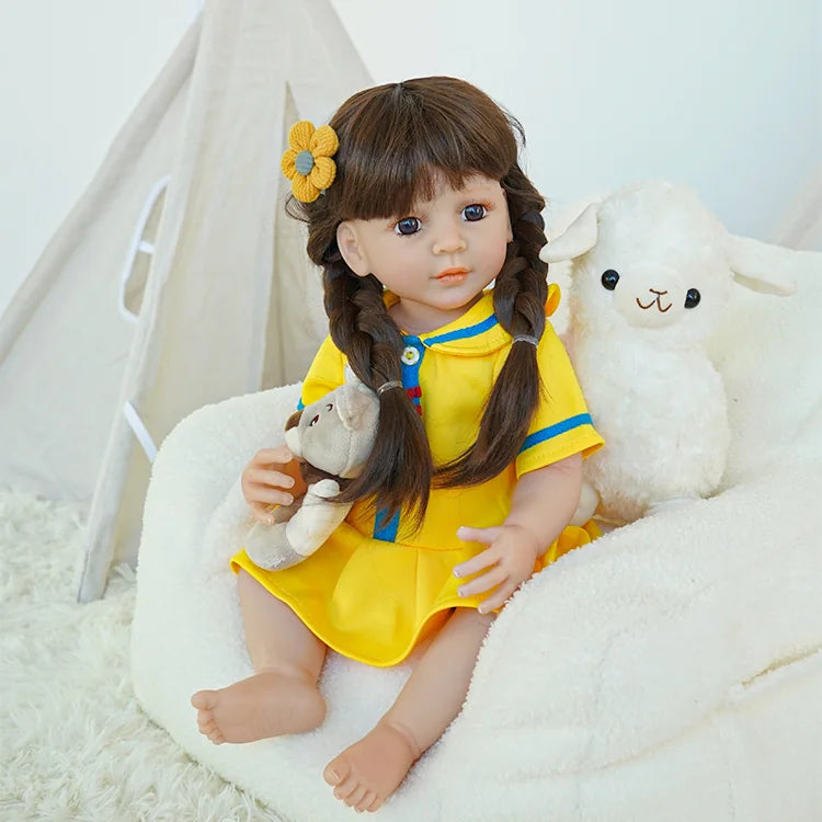 The reborn baby doll in a yellow dress, sitting on a soft chair with a teddy bear and a plush sheep, showing a charming pose.