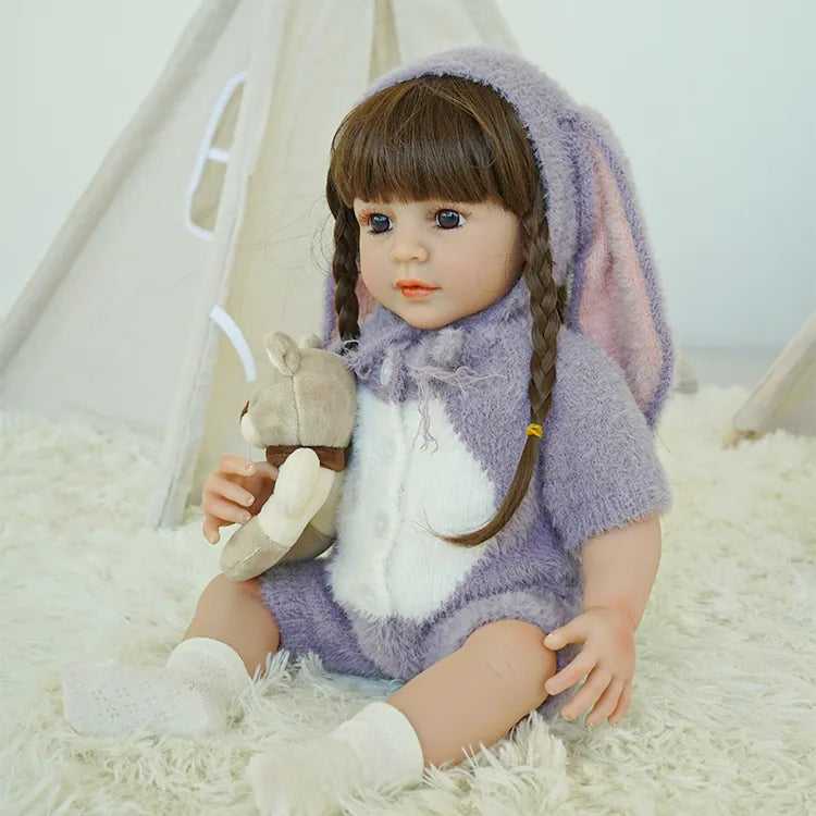 Reborn doll in purple bunny outfit, sitting on the carpet with a teddy bear.