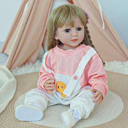 Reborn toddler doll sitting on a soft rug, wearing a pink top and white overalls, looking ahead with a gentle expression.